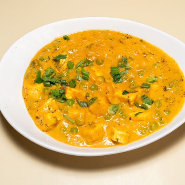 Mutter Paneer, an Indian dish with paneer cheese and peas in a rich orange sauce, garnished with herbs.