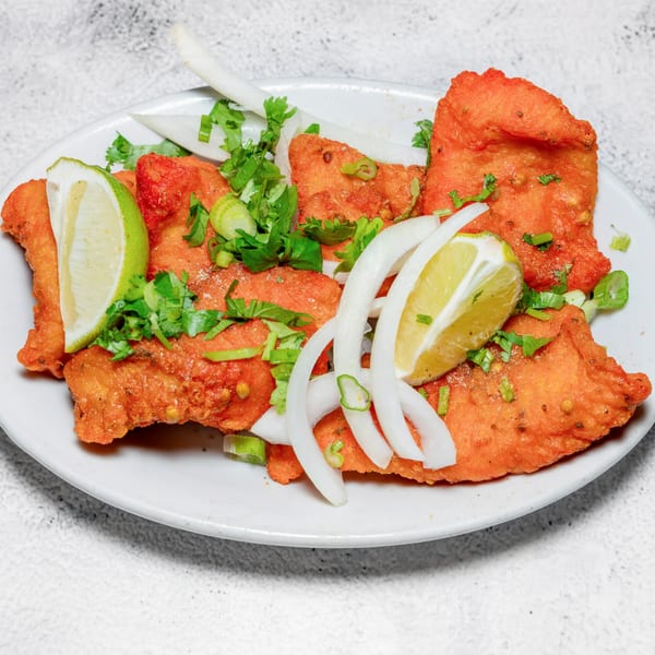 Crispy fried Indian fish pakora, garnished with fresh cilantro, onions, and lime wedges.