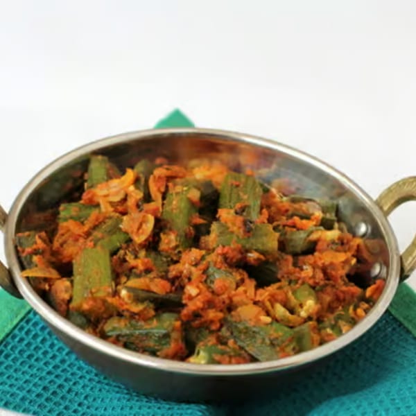Indian okra curry, bhindi masala, in a metal serving bowl on a teal placemat.