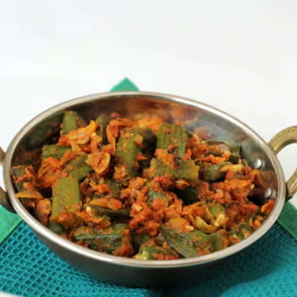 Indian okra curry, bhindi masala, in a metal serving bowl on a teal placemat.