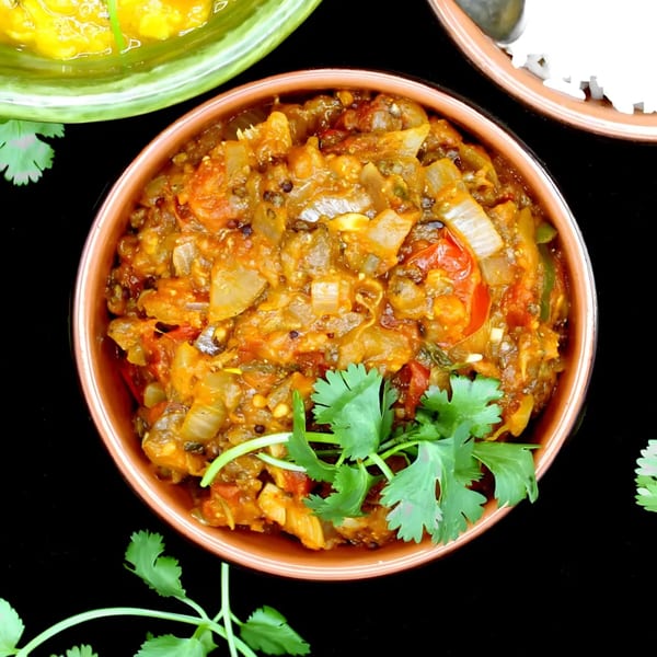 A bowl of Indian eggplant curry with onions and tomatoes, garnished with fresh cilantro.