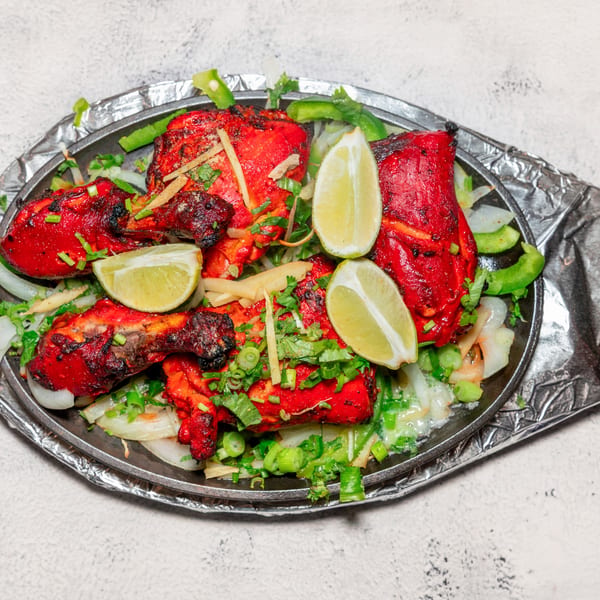 Bright red Indian tandoori chicken with lime, onions, and green herbs on a sizzling platter.