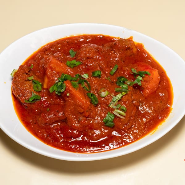 A white bowl filled with a rich red Indian curry, garnished with fresh green herbs.