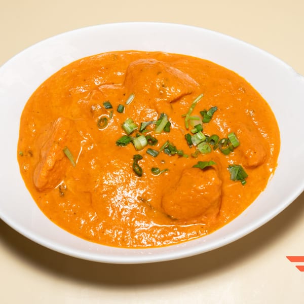 A white bowl filled with orange Indian curry, garnished with chopped green onions.