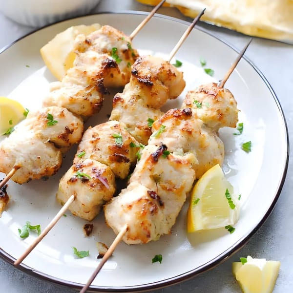 Grilled chicken tikka skewers with lemon wedges and parsley on a white plate.