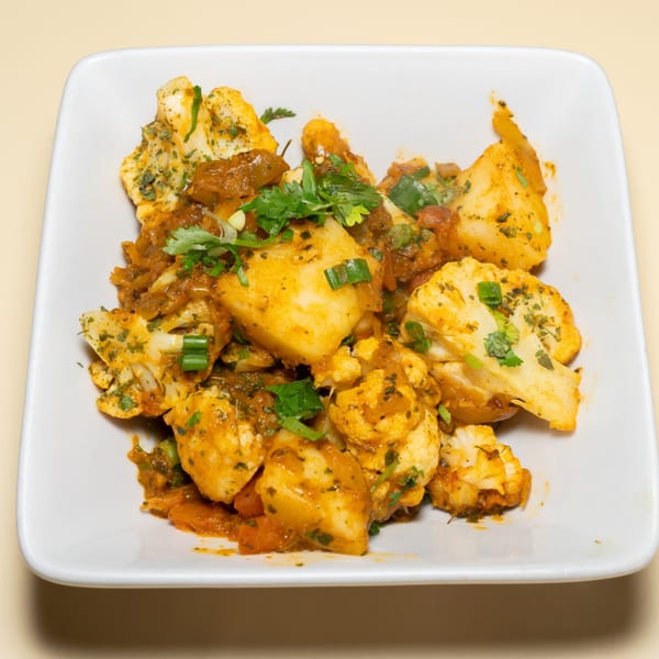 Aloo Gobi, an Indian dish with cauliflower and potatoes in a rich, orange sauce, garnished with cilantro.