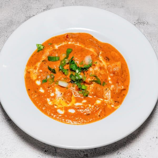 Indian butter chicken or paneer in a rich orange sauce, garnished with fresh herbs and cream swirls.