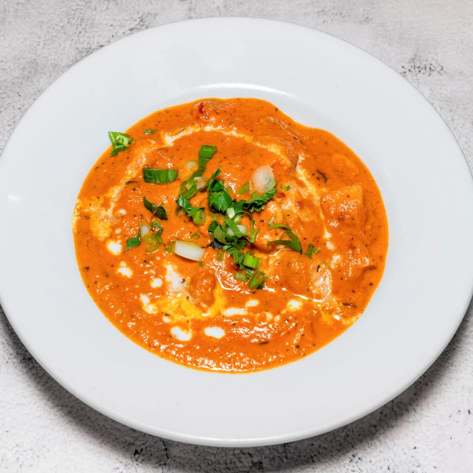 Indian butter chicken or paneer in a rich orange sauce, garnished with fresh herbs and cream swirls.