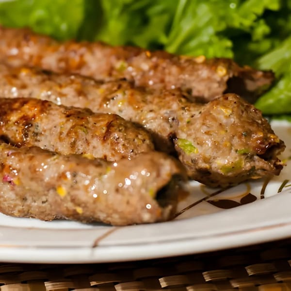 Four Indian seekh kebabs, garnished with green lettuce, on a white plate with gold trim.