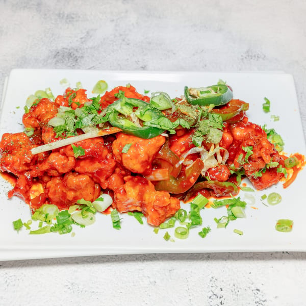 Spicy Indian chili chicken, garnished with green onions, cilantro, and sliced jalapeños on a white plate.