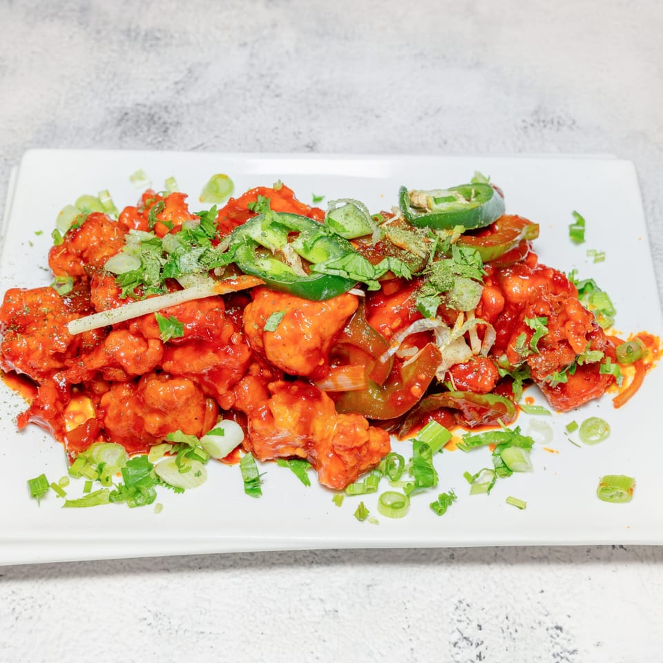 Spicy Indian chili chicken, garnished with green onions, cilantro, and sliced jalapeños on a white plate.
