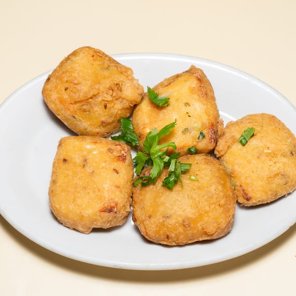 Five golden-brown Indian paneer pakora, garnished with fresh cilantro, on a white oval plate.