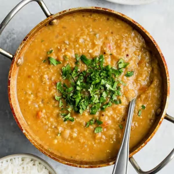 A copper pot of Indian dal, garnished with fresh cilantro, with a spoon and rice.